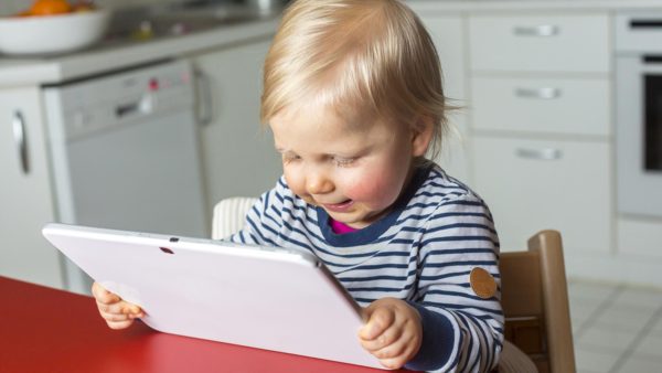 A toddler looks at an iPad while sitting in a high chair.